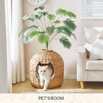 Woven rattan cat house cave topped with an artificial green palm plant, with a white cat looking out inside a living room.