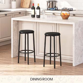 Set of 2 modern black padded bar stools with metal frames placed by a wooden kitchen island bar counter.