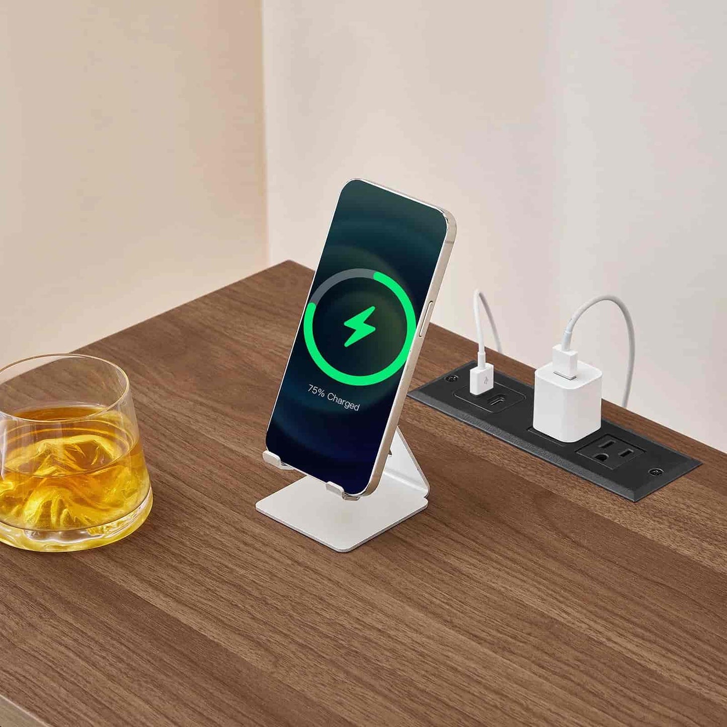 Wireless phone charger on a wooden desk with a glass of juice and a power strip.