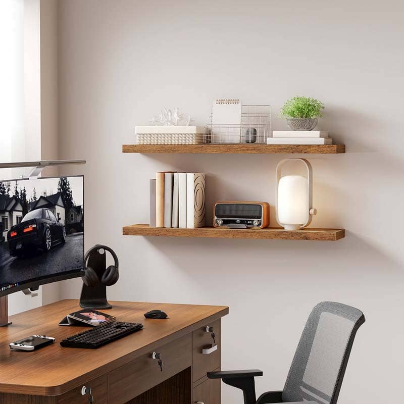 Two rustic brown floating shelves mounted on a wall above an office desk holding books and a lamp.