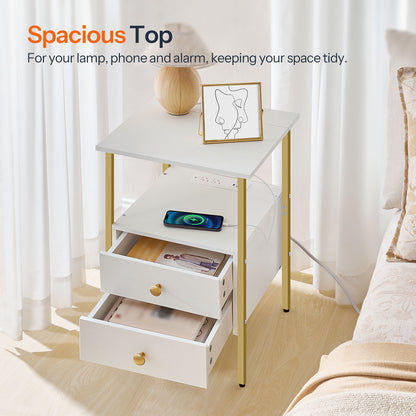 White nightstand with gold legs and drawers, featuring a lamp, phone, and alarm clock in a bedroom setting.
