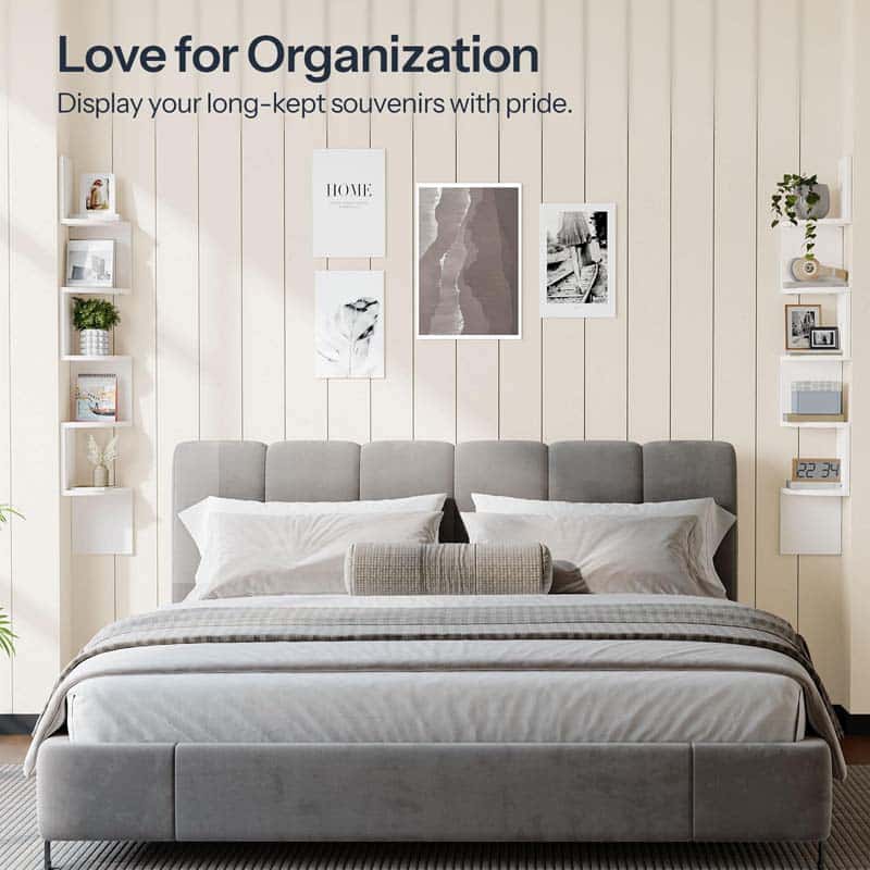 Gray upholstered bed with white bedding in a room with shelves and framed pictures on the wall.