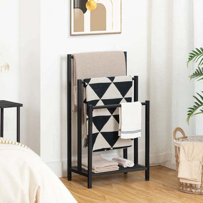 A black metal multi-tier towel rack styled in a bedroom setting, holding a beige patterned throw blanket, a black and white geometric blanket, and a white towel.