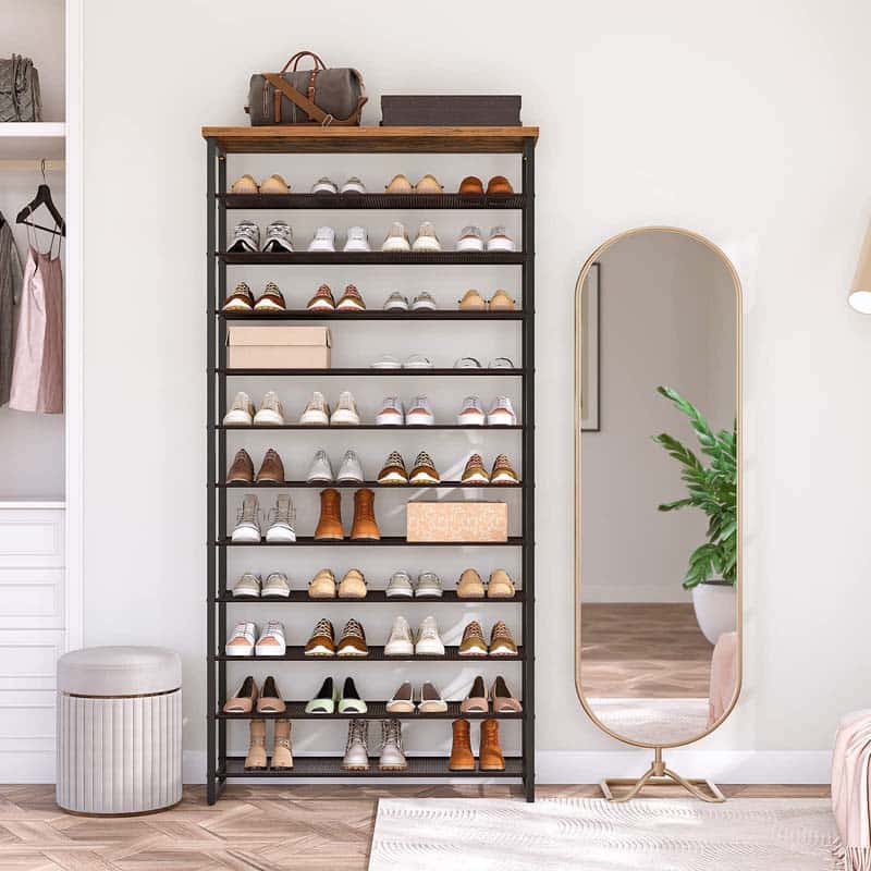 Shoe rack with various shoes, standing mirror, and plant in a room setting.