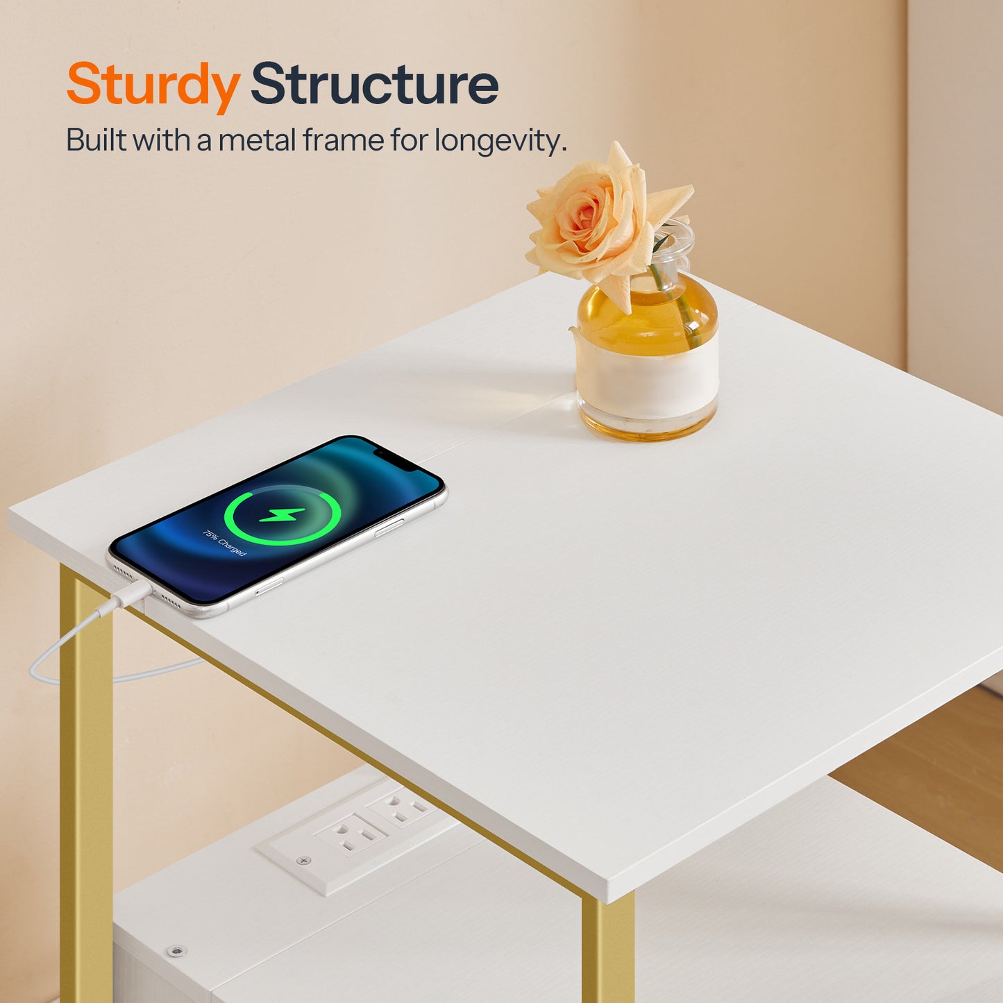 Small white table with gold legs, charging phone, and vase with flowers on a beige background.