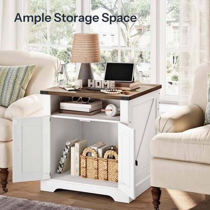 A white side table with a dark wood top and two open cabinet doors, styled in a bright living room between two cream armchairs. The table holds a lamp, books, a small monitor, and baskets underneath.