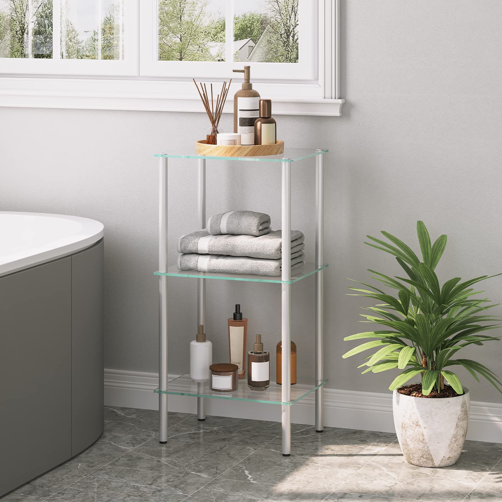 Glass shelf unit in a bathroom with towels and bottles on a gray floor.