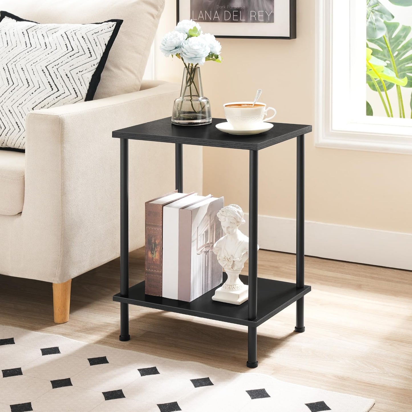 Black side table with books, a cup, and a vase in a living room setting.