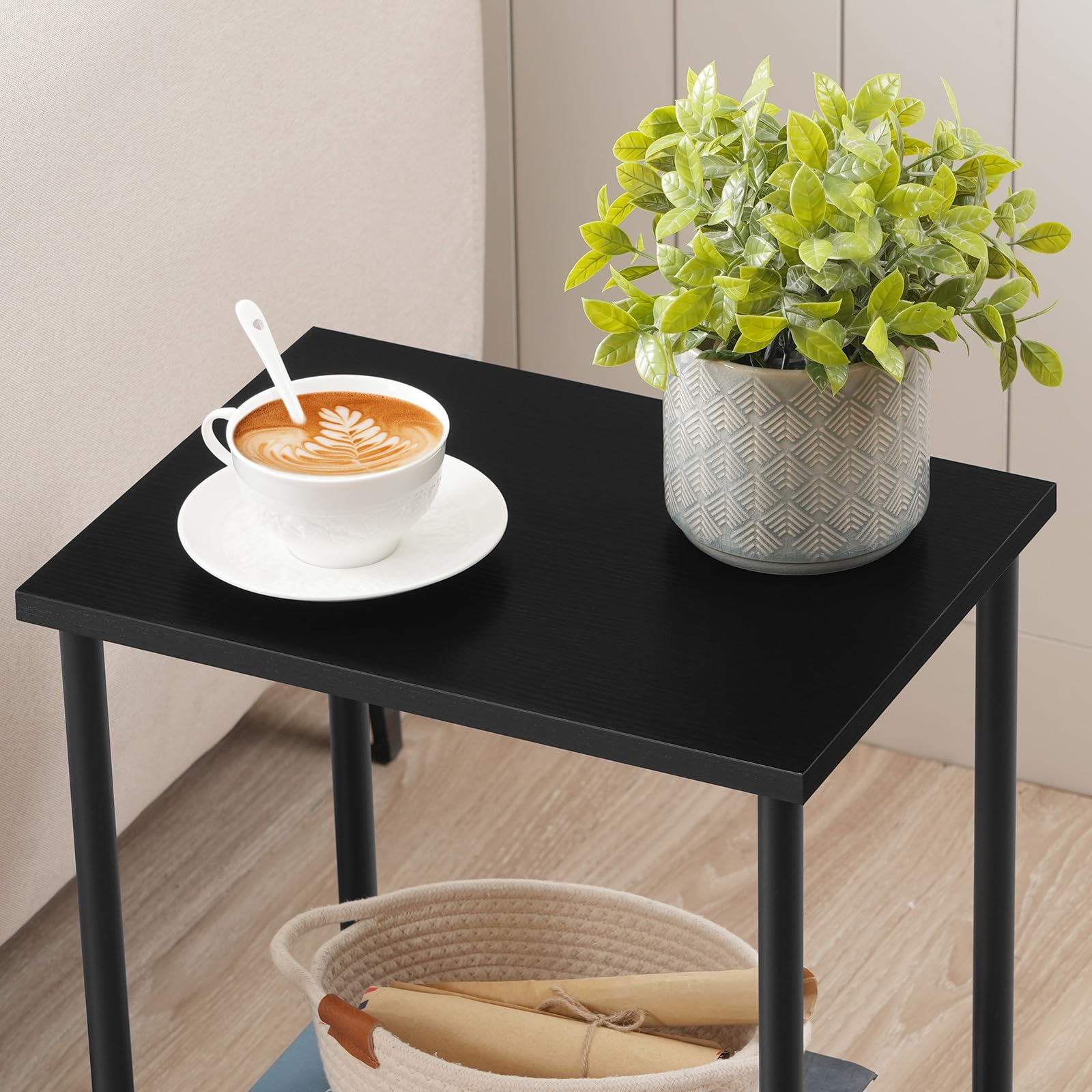 Black side table with a cup of coffee, saucer, and plant on a wooden floor.