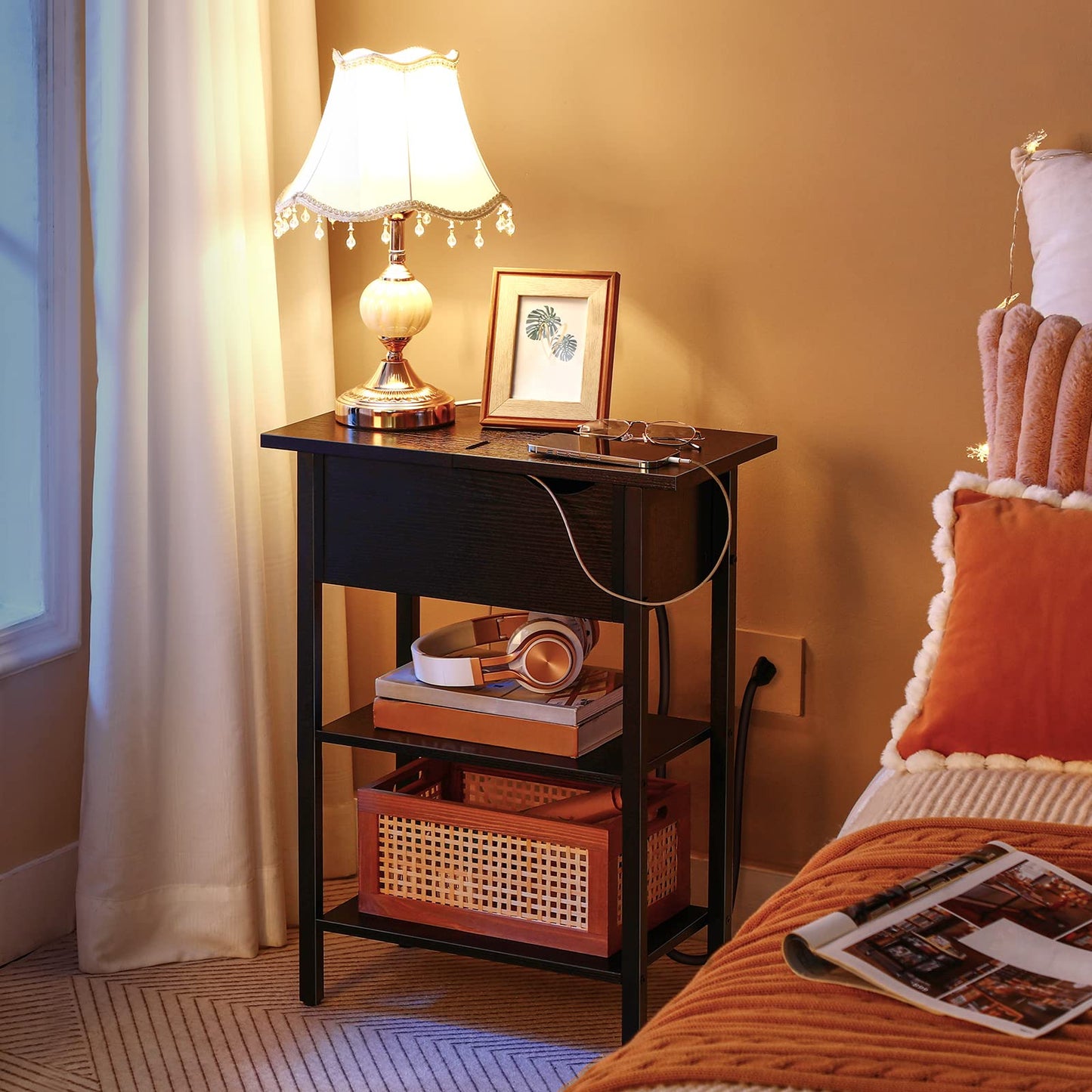 Small wooden side table with lamp, books, and headphones next to a bed with orange bedding.