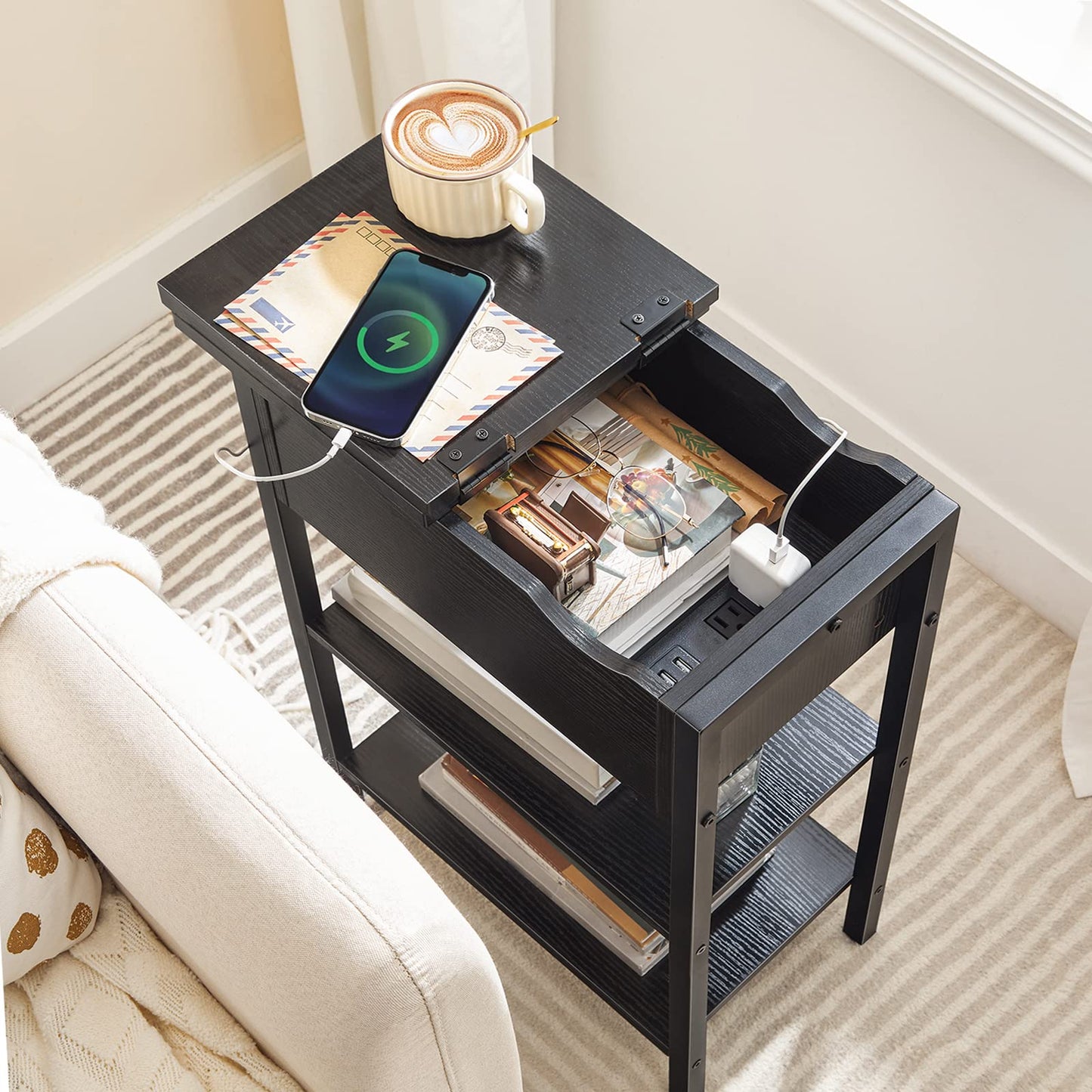 Black side table with open drawer, phone charging, and a cup of coffee on top.