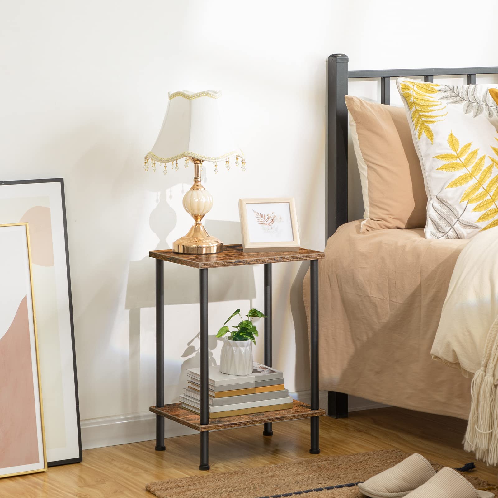Small wooden side table with lamp and decor items next to a bed with pillows and blankets.