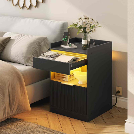 Black nightstand with yellow illuminated drawer next to a bed
