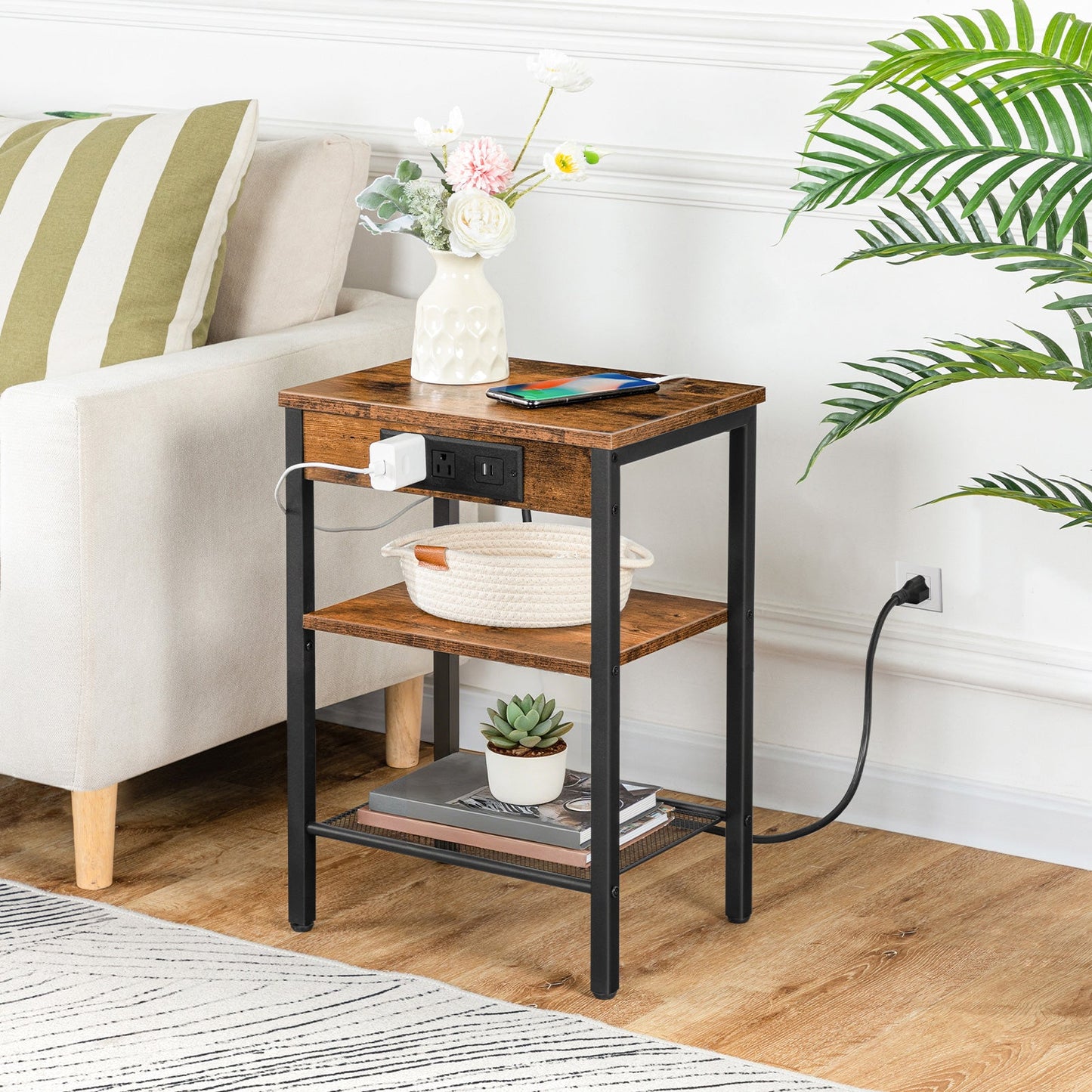 Rustic brown 3-tier side table with built-in charging station holding a flower vase next to a sofa.