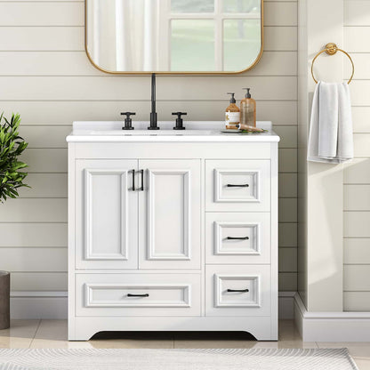 A white single-sink bathroom vanity cabinet with black hardware, shown in a styled bathroom setting with a white shiplap wall, gold-framed mirror, black faucet, and a white towel on a gold ring holder.