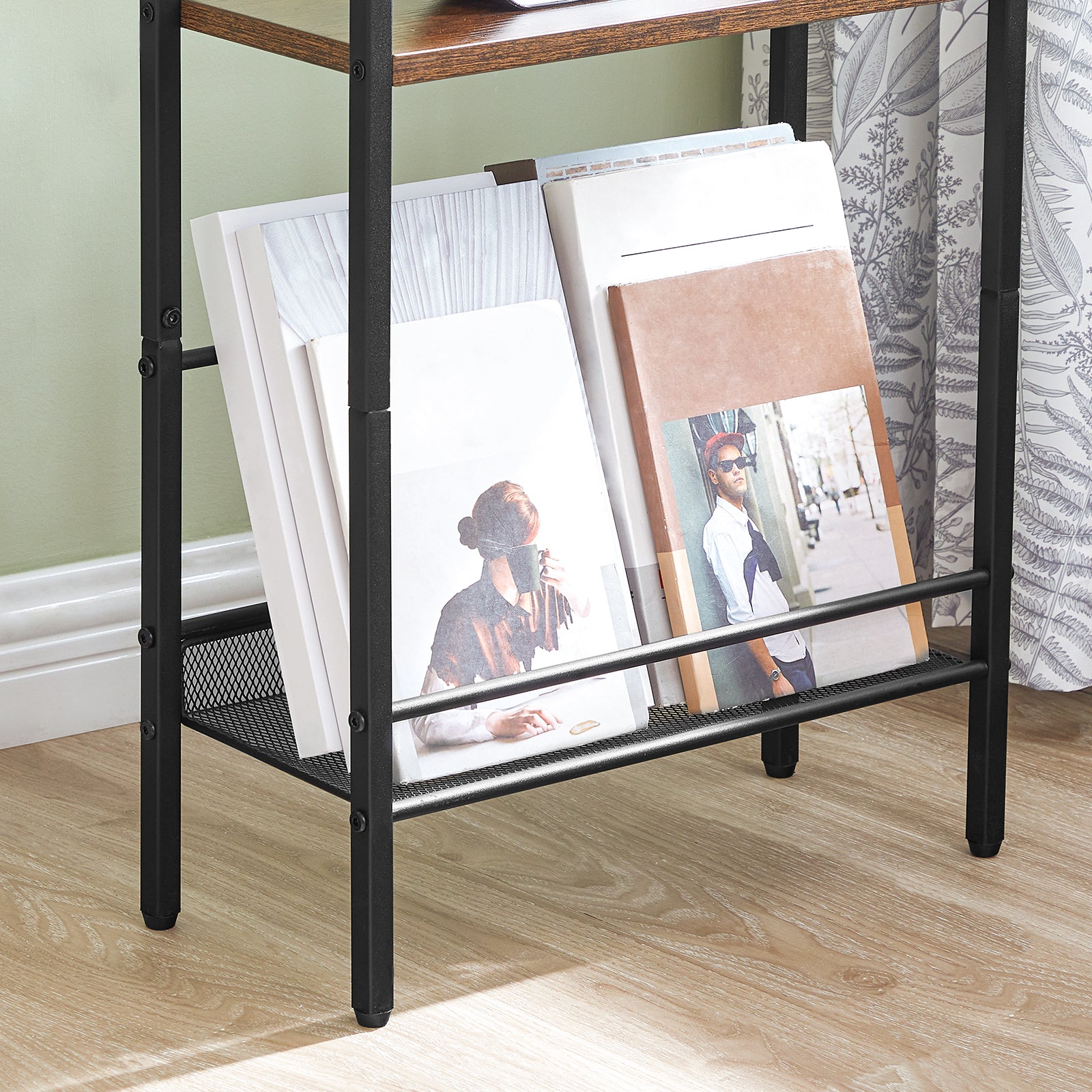 Black metal magazine rack with books on a wooden floor against a light green wall.
