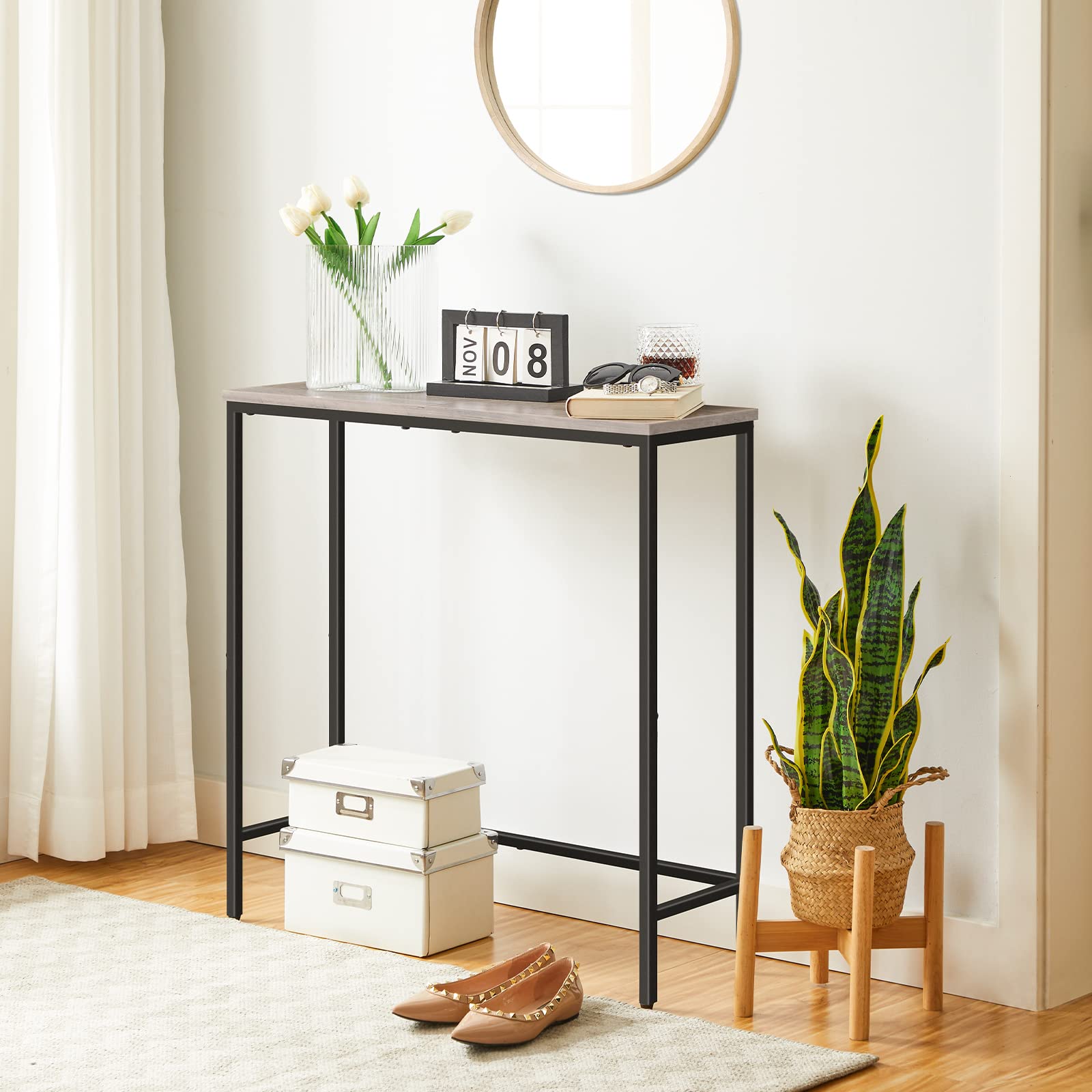 Console table in a room with decor items including a plant, calendar, and shoes.