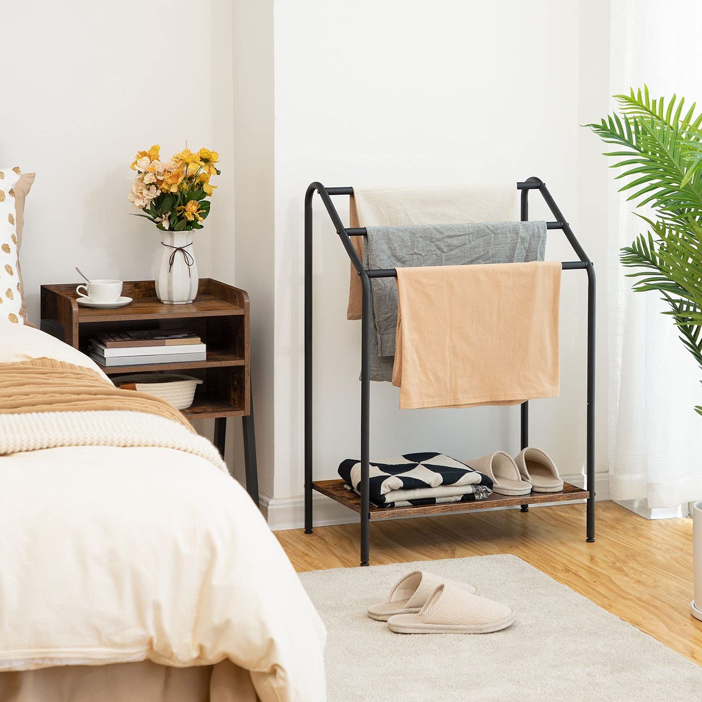 Black metal clothing rack with folded clothes in a bedroom setting.
