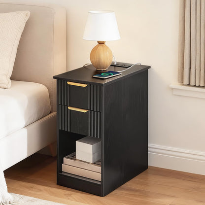 Black nightstand with lamp and books next to a bed in a bedroom.