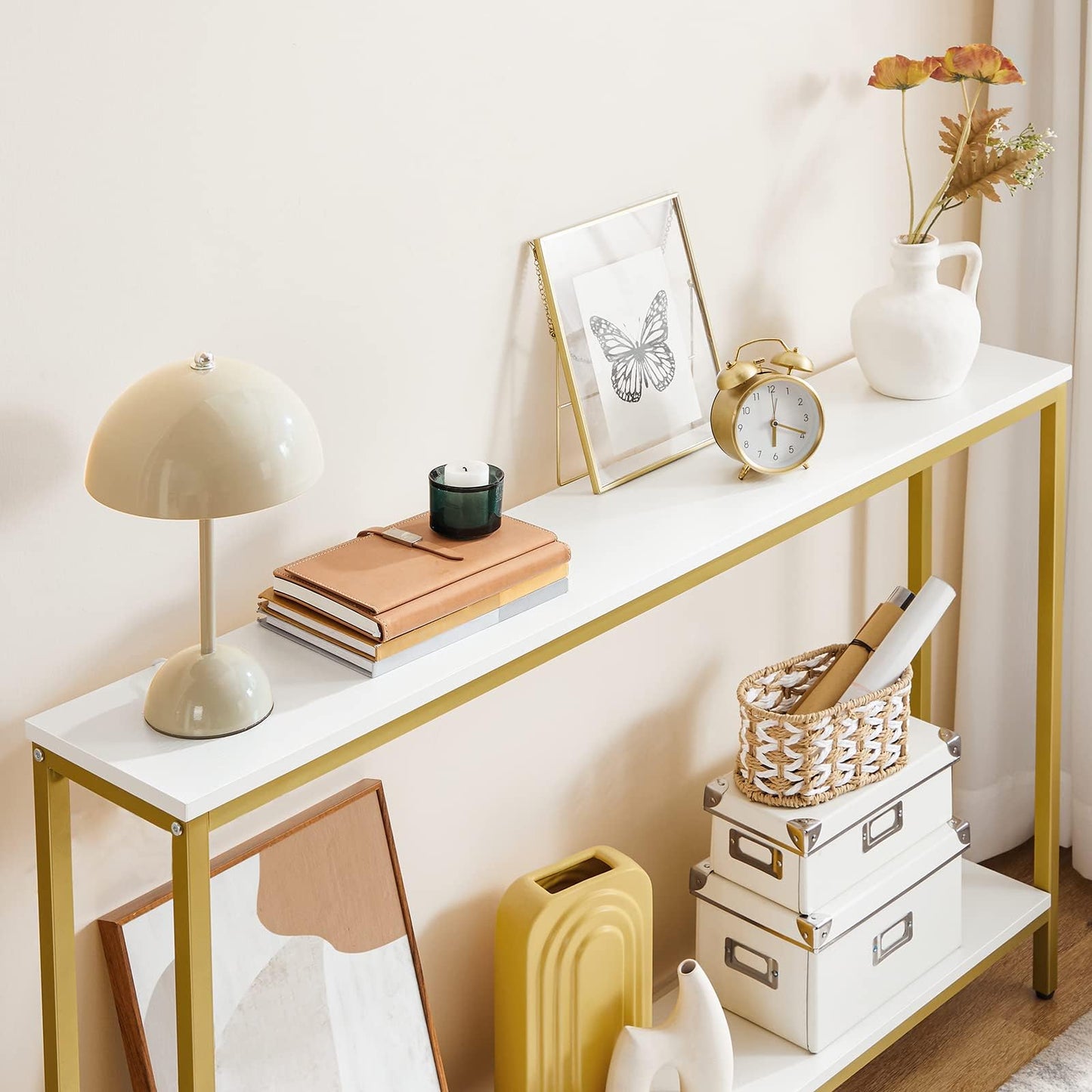 White console table with gold legs, decorative items including a lamp, books, and a clock, against a light wall.