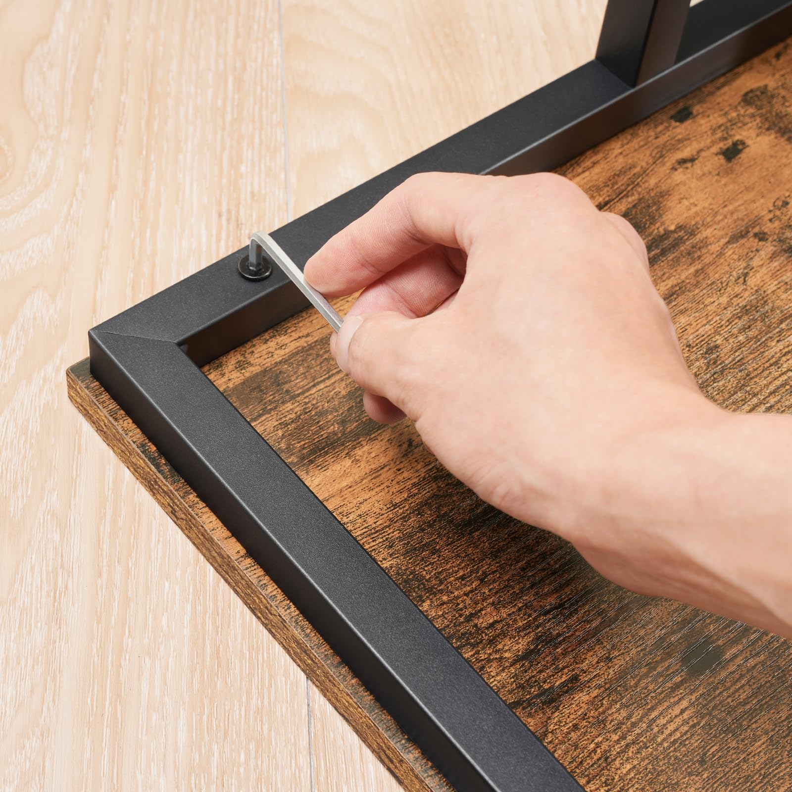Hand using a screwdriver to assemble a wooden shelf with metal brackets.