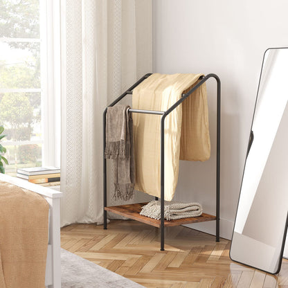 Black metal towel rack with wooden shelf holding towels in a bedroom.