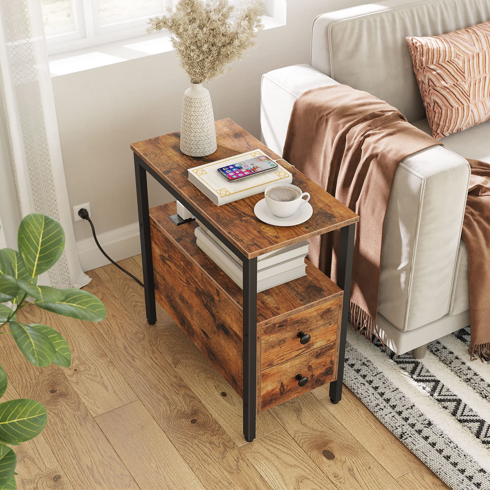 Wooden side table with a smartphone, mug, and books next to a white sofa with a blanket and pillow.