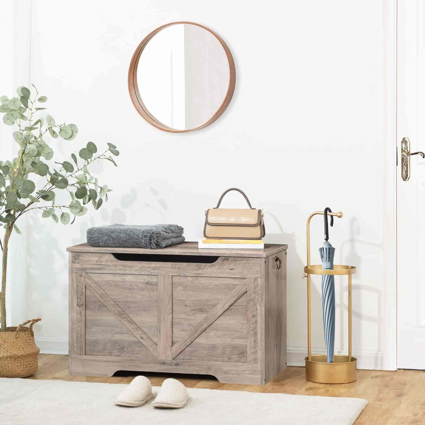 Wooden storage bench with a round mirror above, plant to the left, and umbrella stand on the right.