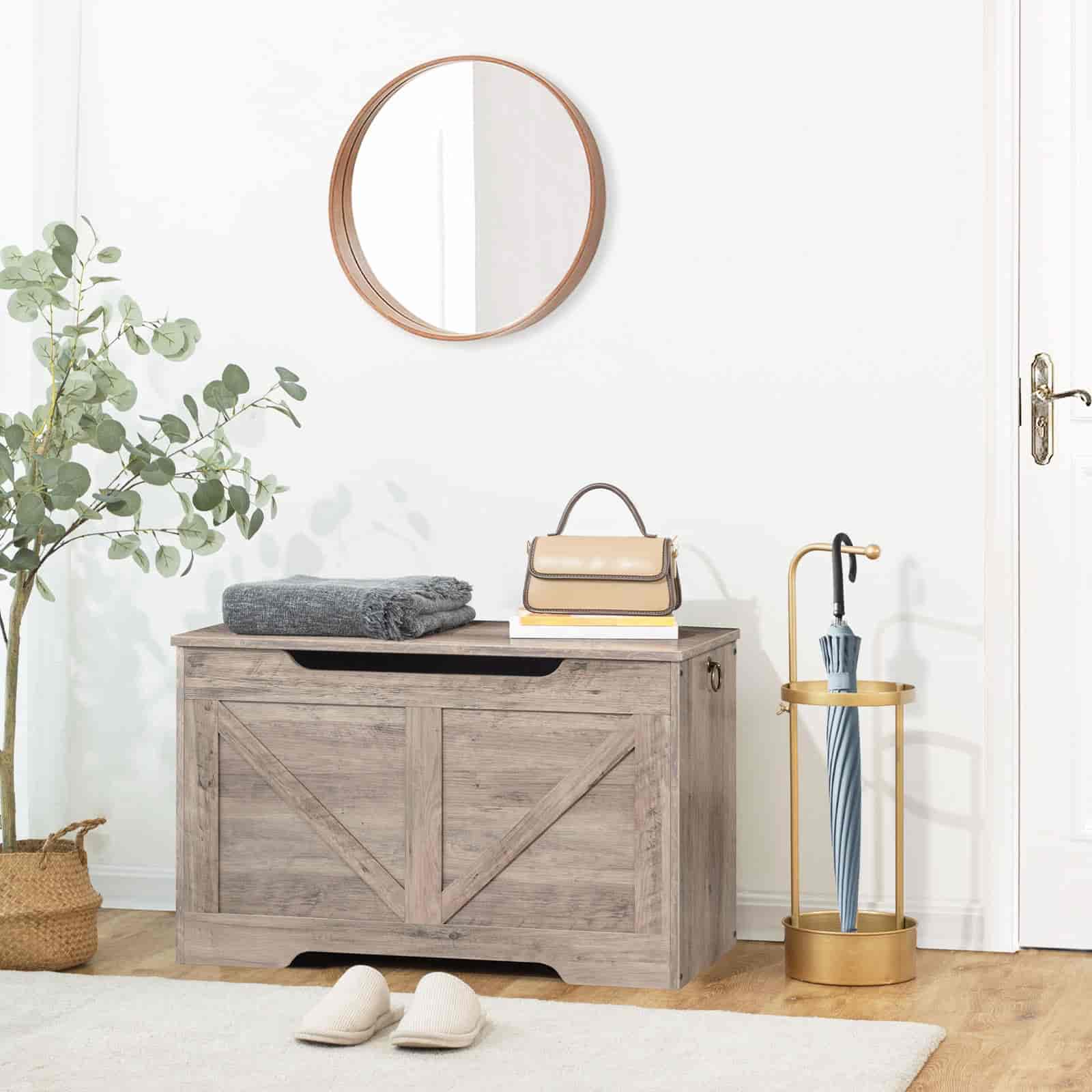 Wooden storage bench with a round mirror above, plant to the left, and umbrella stand on the right.