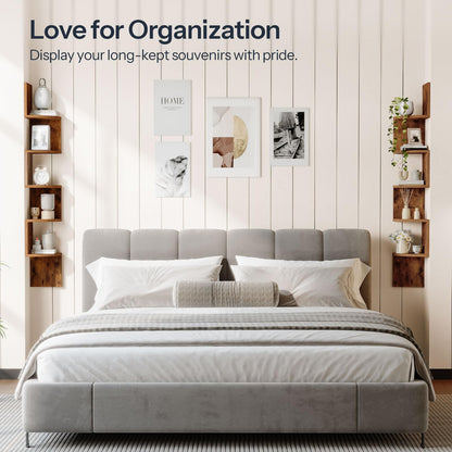 Gray upholstered bed with white bedding in a room with wooden shelves and framed pictures on the wall.