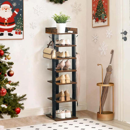 A tall, narrow wooden shoe rack with a black metal frame stands in a decorated entryway. The rack has five shelves, some of which are styled with shoes, handbags, and a potted plant, and features side hooks holding umbrellas.