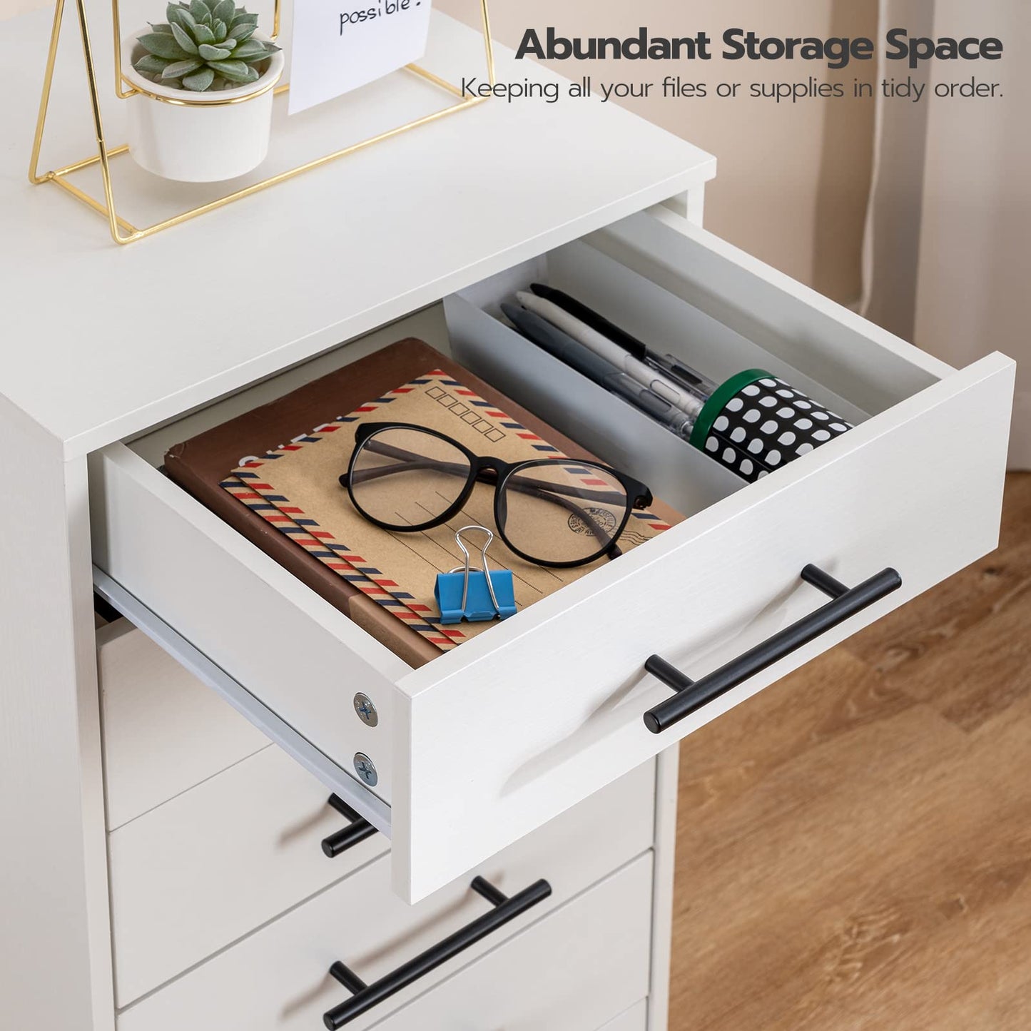 Open drawer of a white desk with office supplies on a wooden floor.
