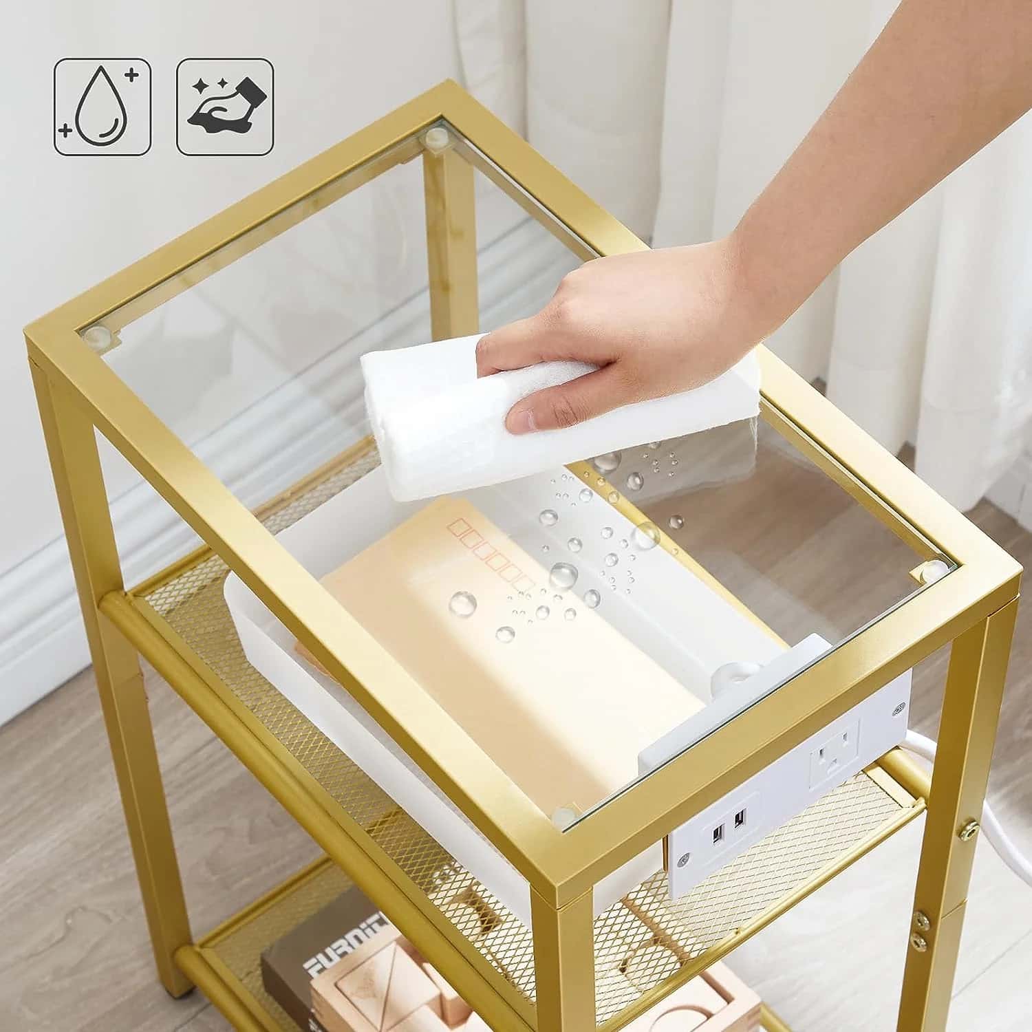 Person cleaning a glass-top gold metal table with a white cloth.