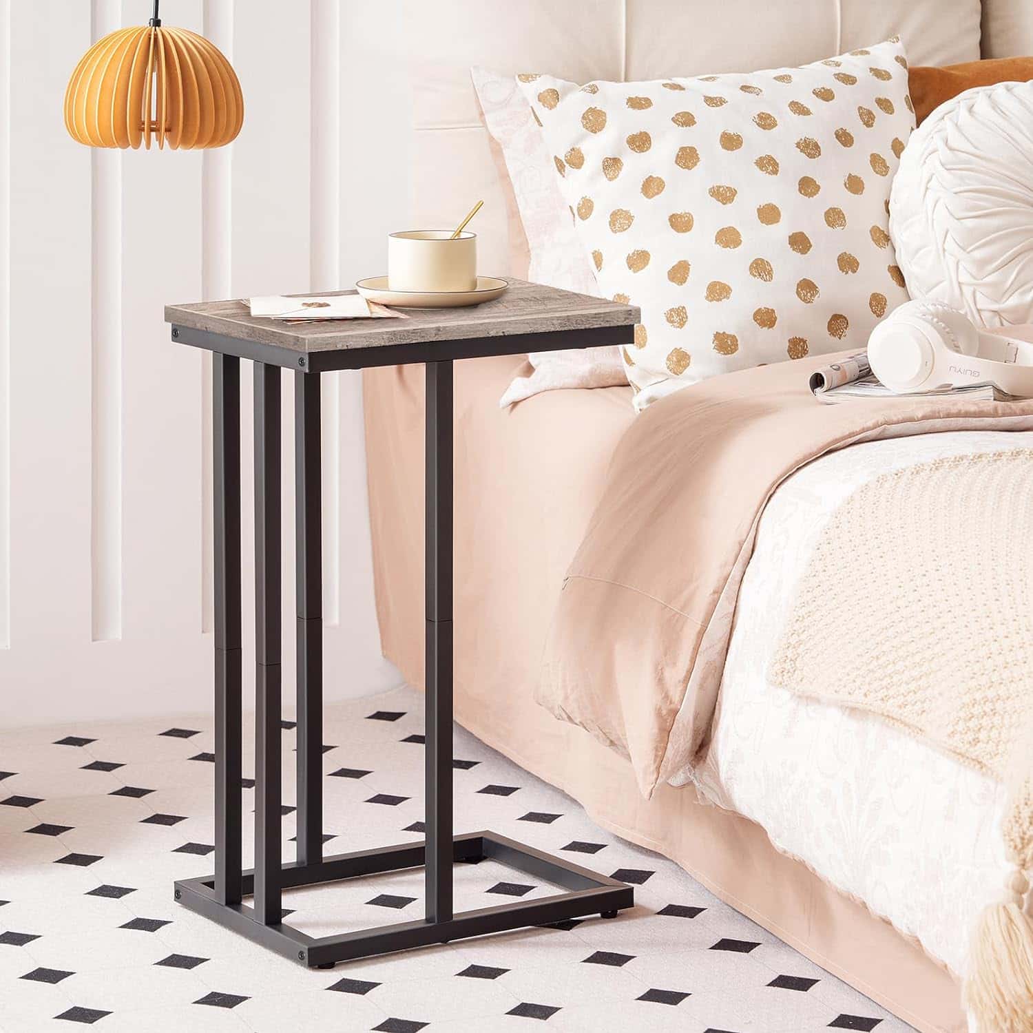 Small side table next to a bed with decorative pillows and a lamp.