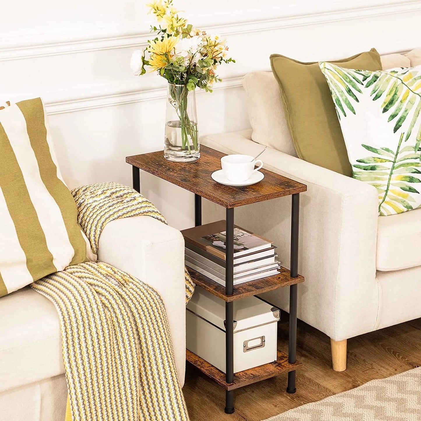 Small wooden side table with books and a cup next to a white sofa with green and yellow pillows.
