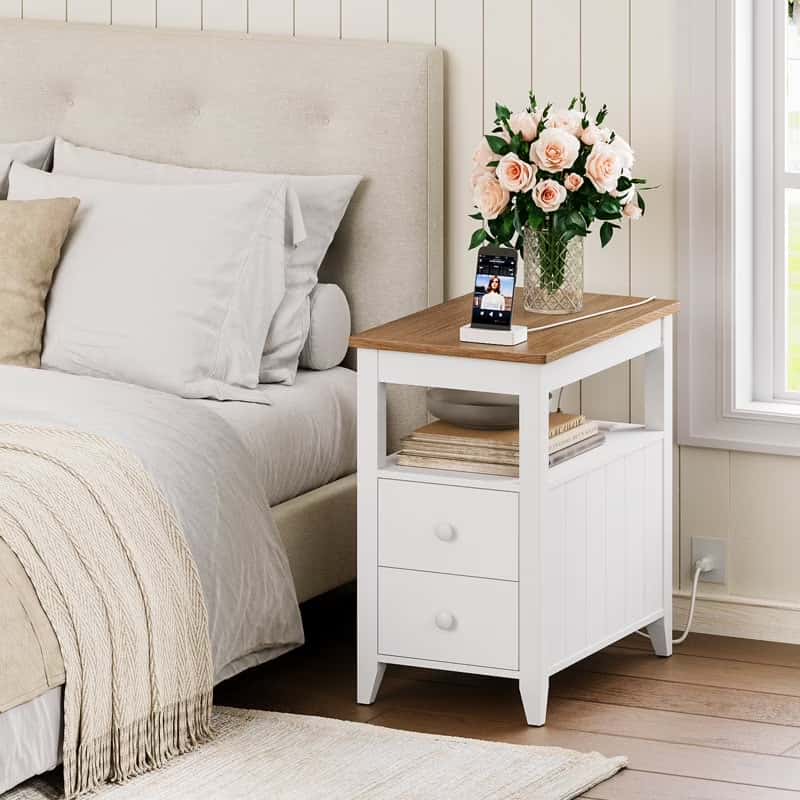 White nightstand with wooden top next to a bed with beige bedding.