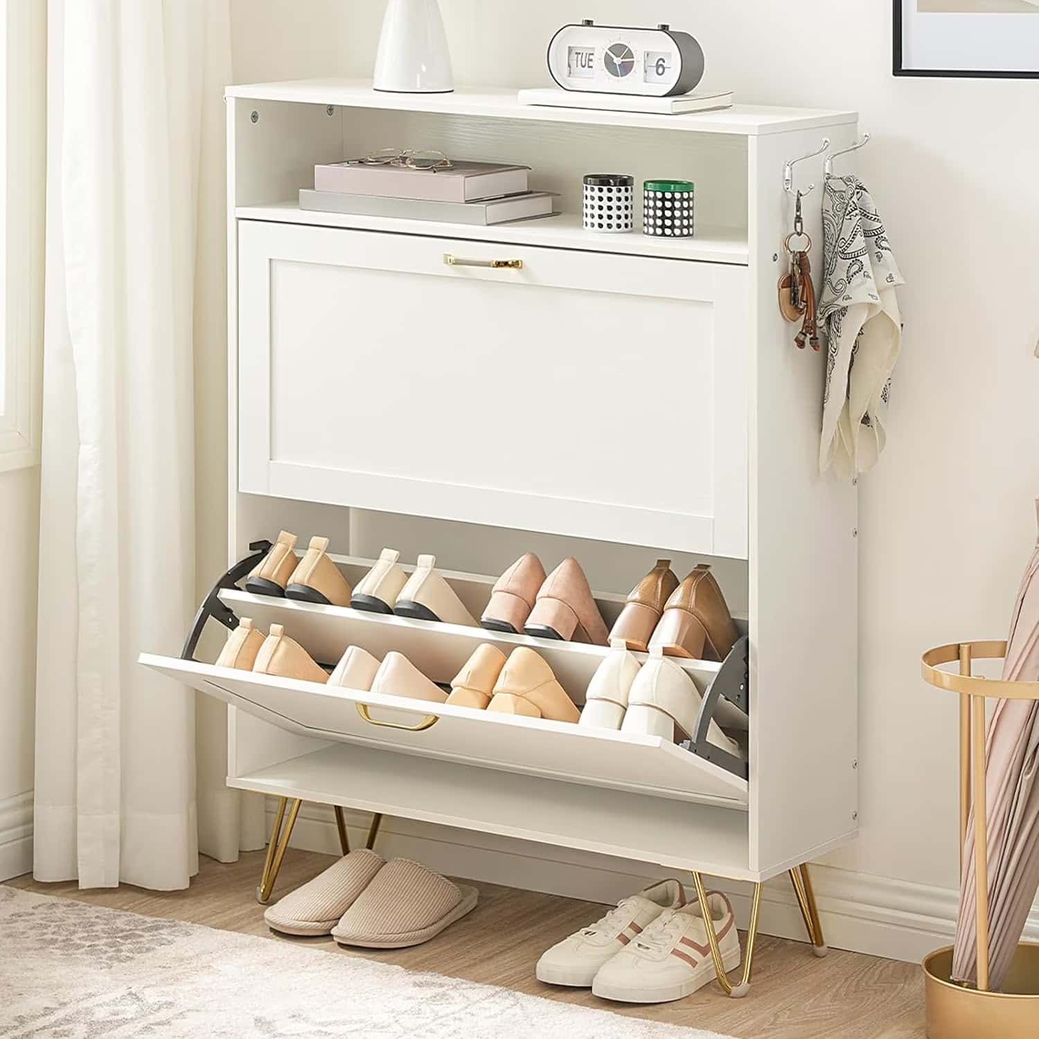White shoe cabinet with open door displaying shoes, books, and a clock on a wooden floor.