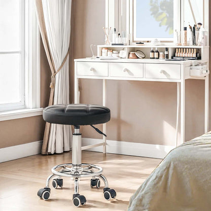 Black stool with wheels in a room with a white desk and window.
