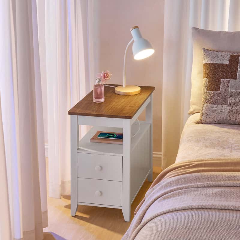 White nightstand with wooden top next to a bed with a lamp and small plant.