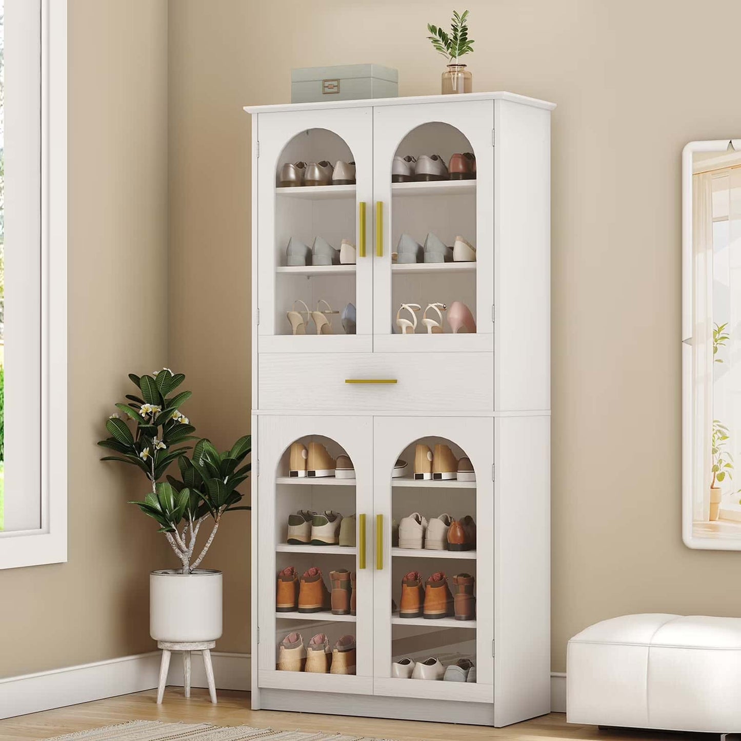 White cabinet with glass doors displaying various items in a room with a plant and ottoman.