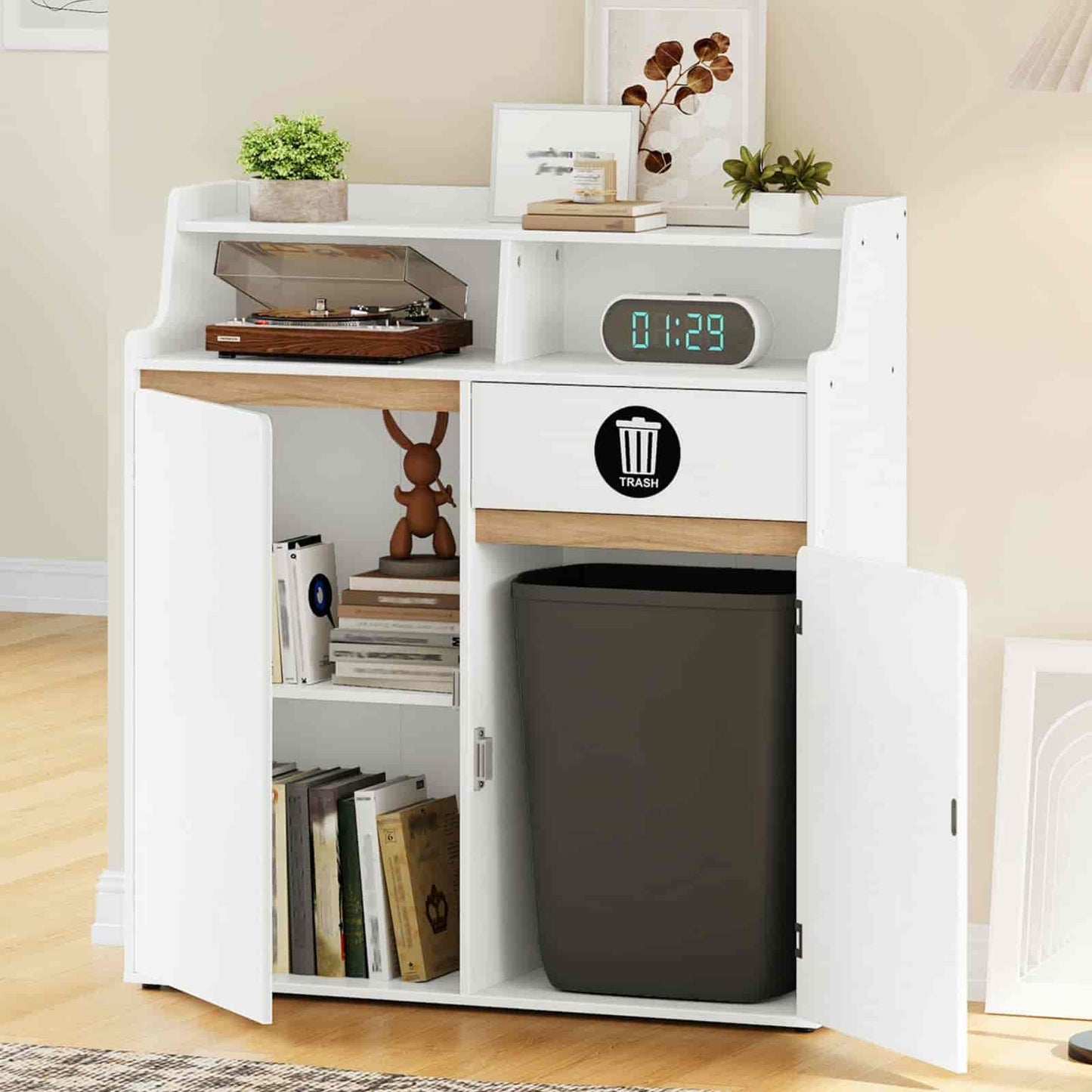 White storage unit with a trash can inside, books, and decorative items on a wooden floor.