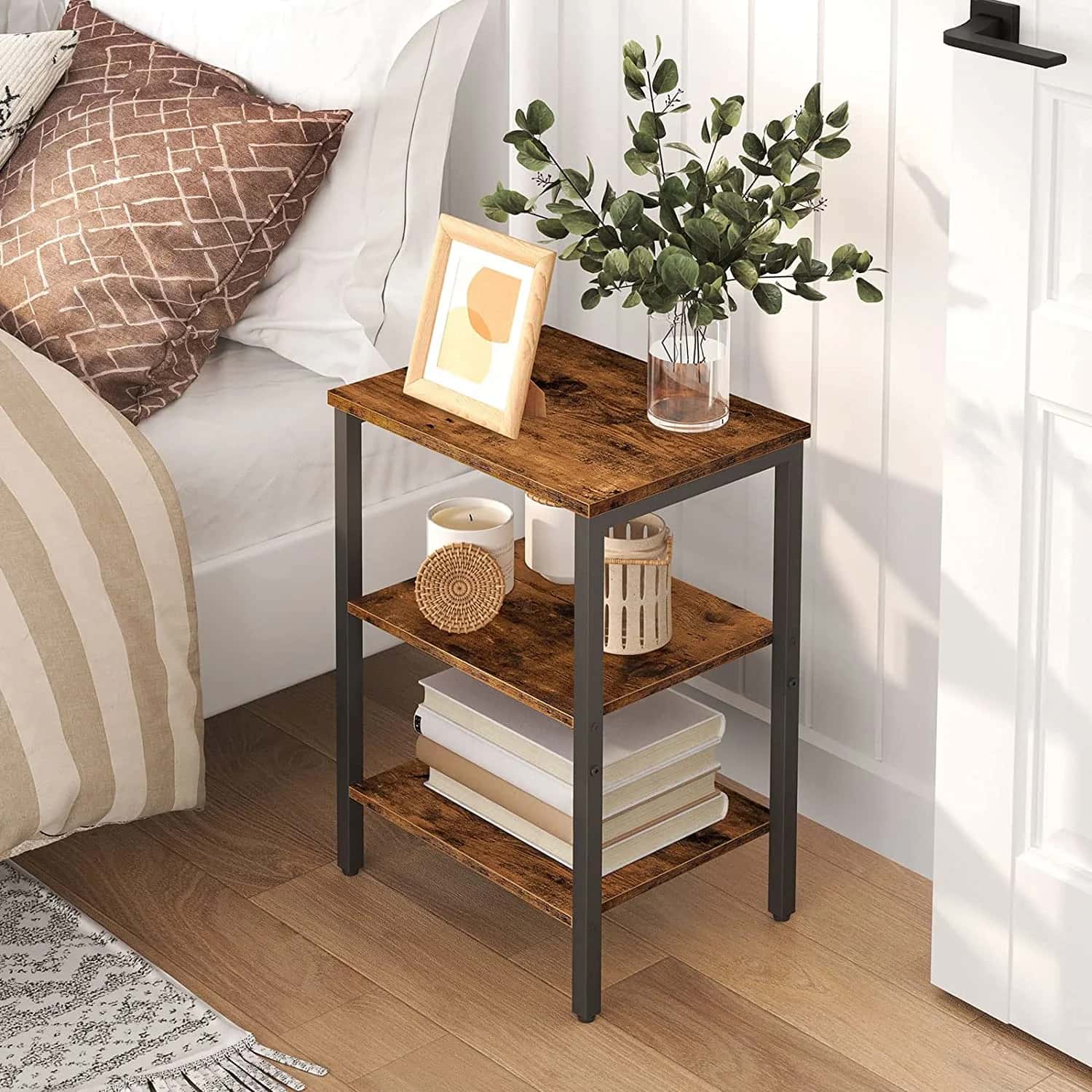 Wooden side table with books, candles, and a plant in a room with a couch and rug.