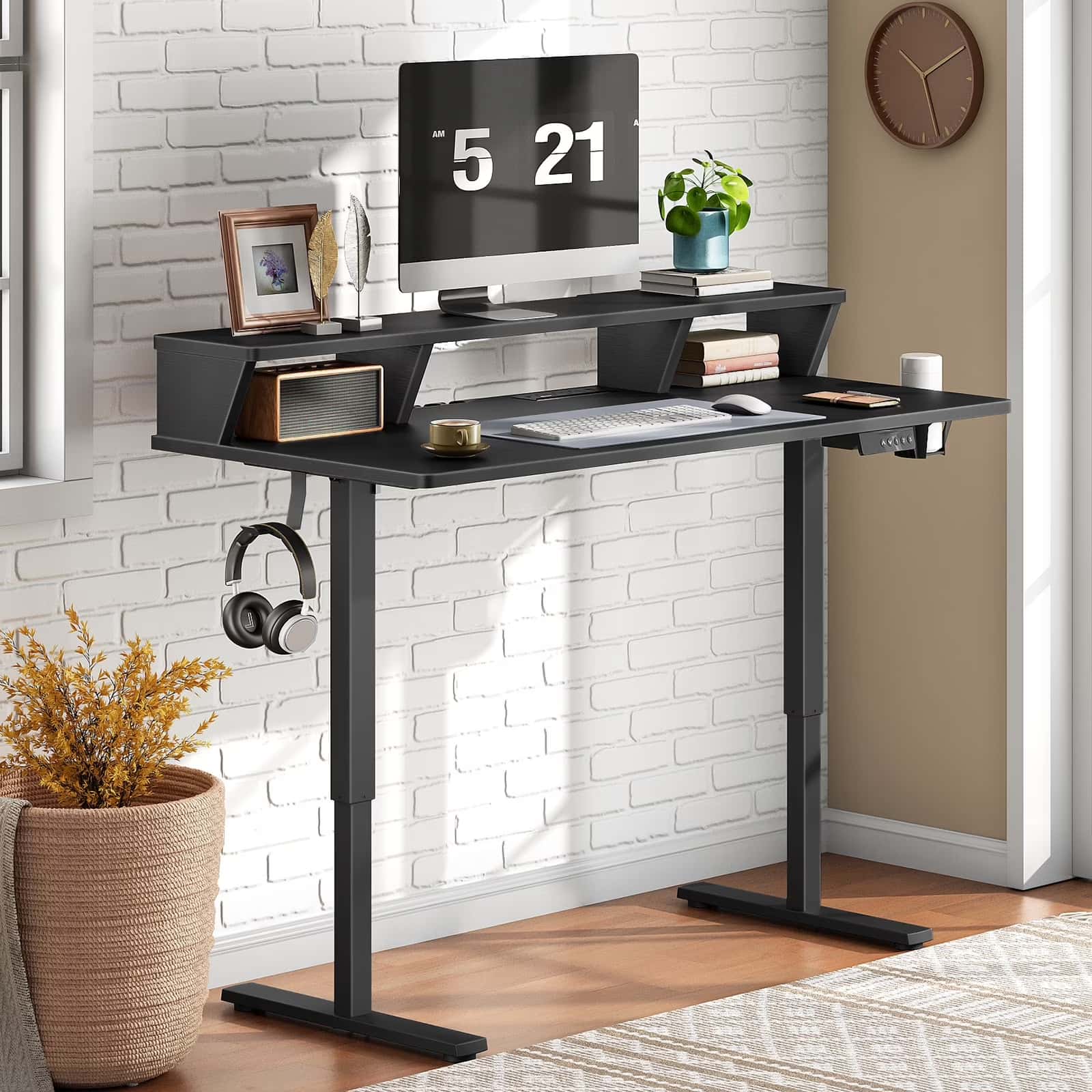 Black computer desk with a monitor, keyboard, and other items against a white brick wall.