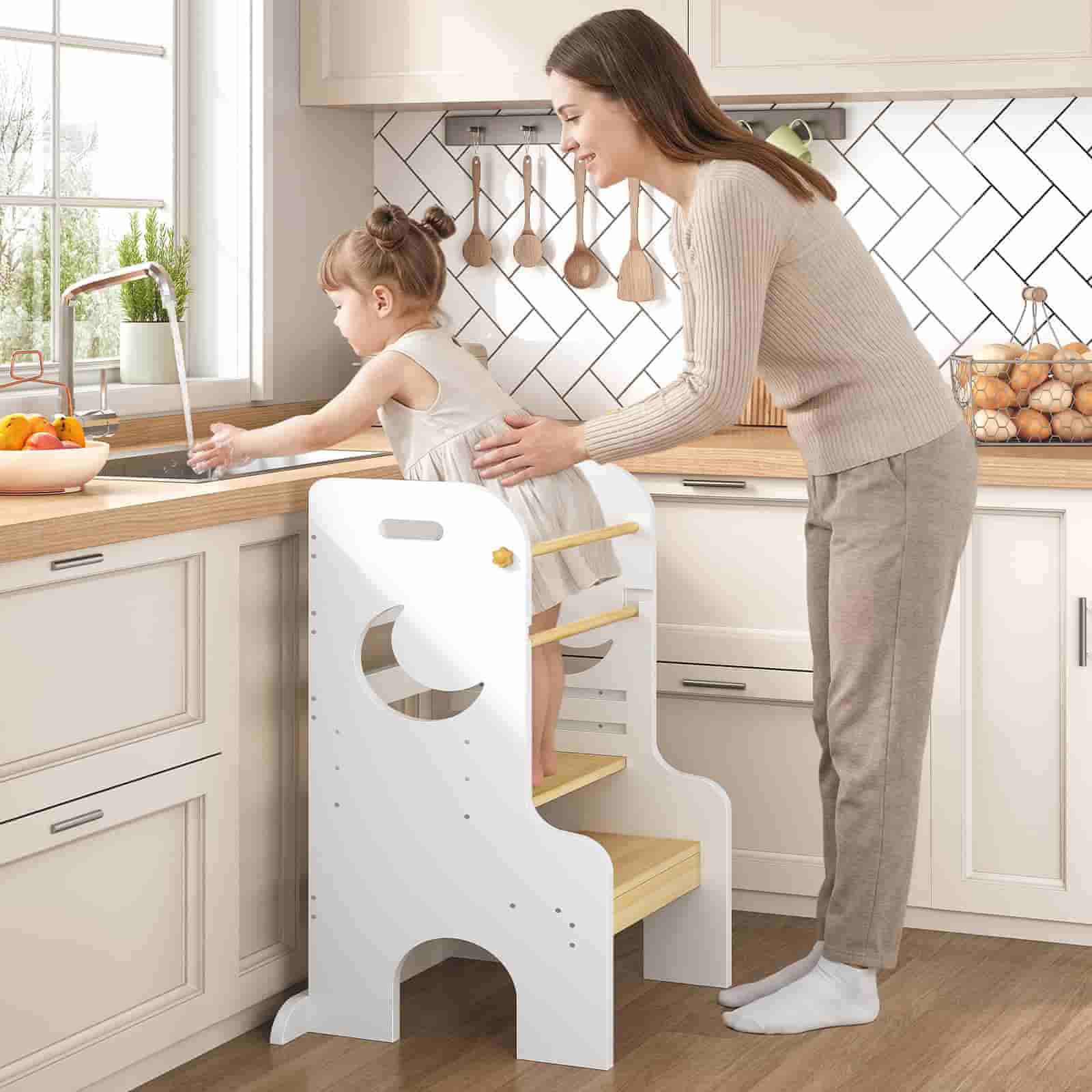 Woman helping a child on a white step stool in a kitchen.