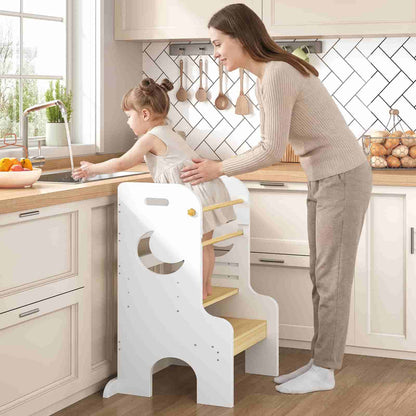 Woman helping a child on a white step stool in a kitchen.