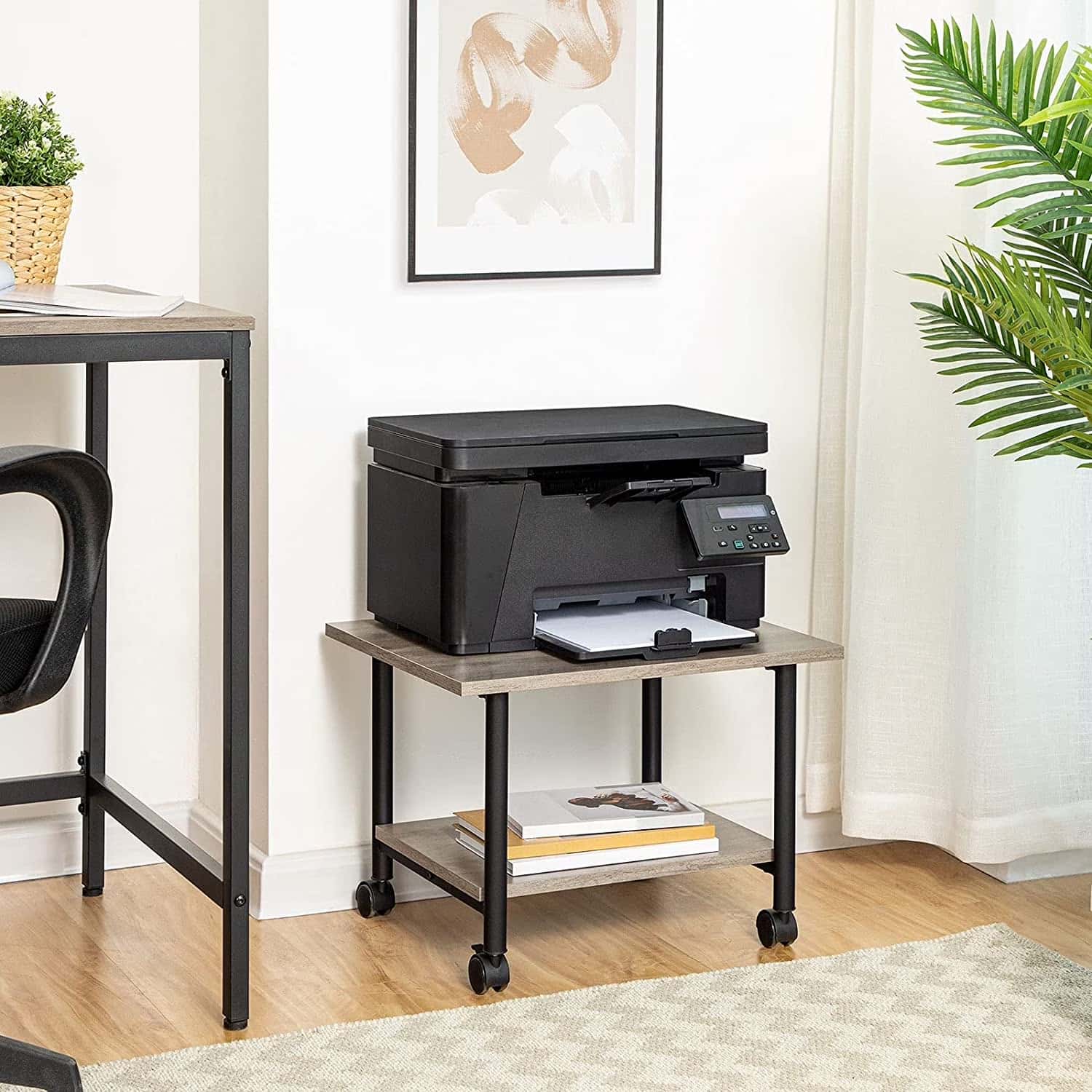 Black printer on a wooden table in a home office setting with a desk and plants.