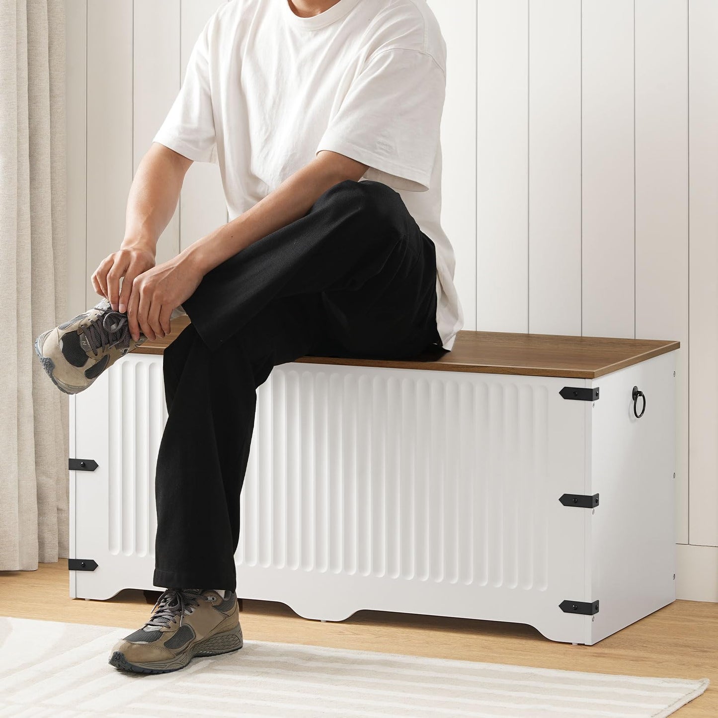 Person sitting on a white storage bench with a wooden top in a room.
