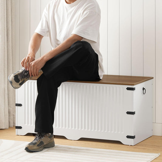 Person sitting on a white storage bench with a wooden top in a room.