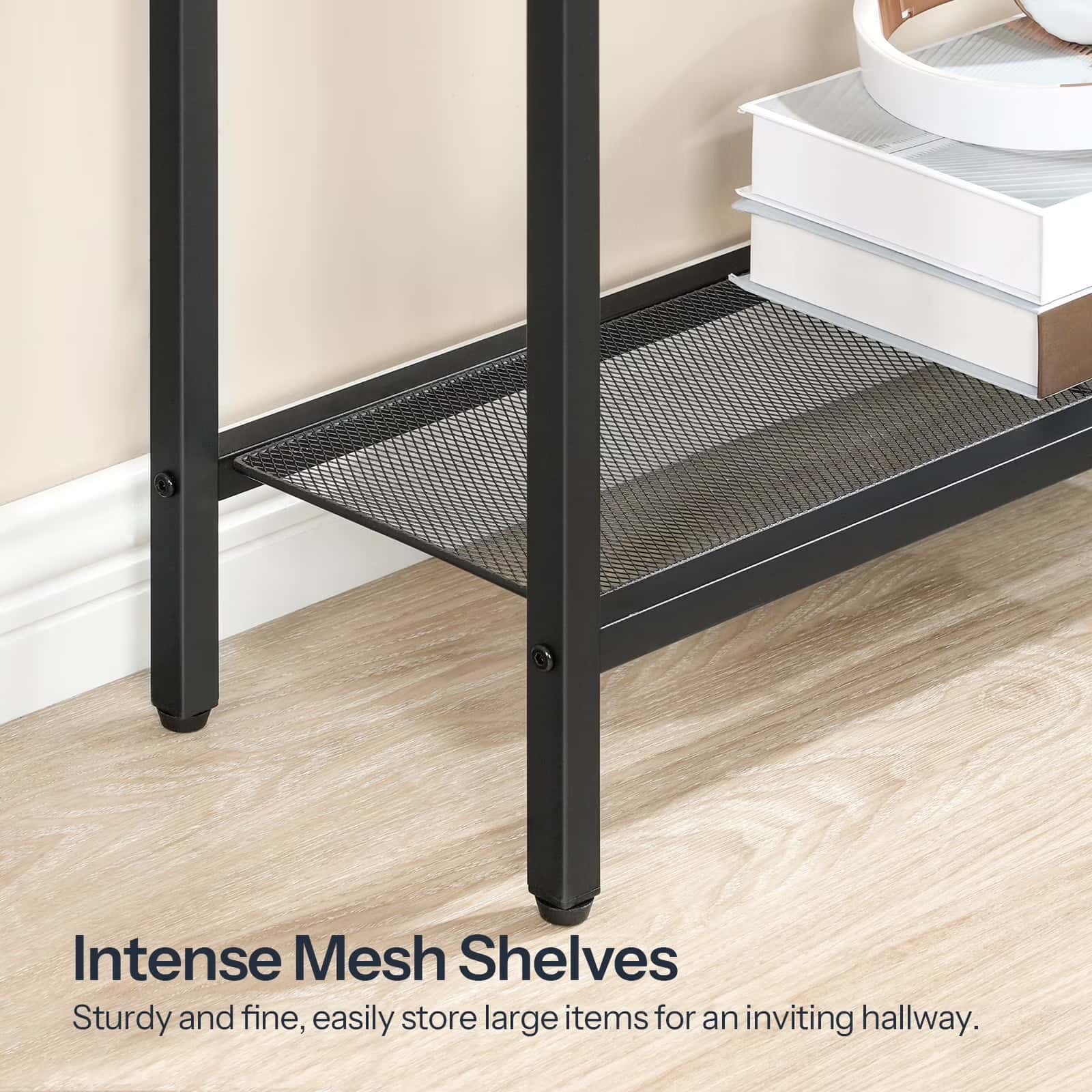 Black mesh shelf with books on a wooden floor against a beige wall.