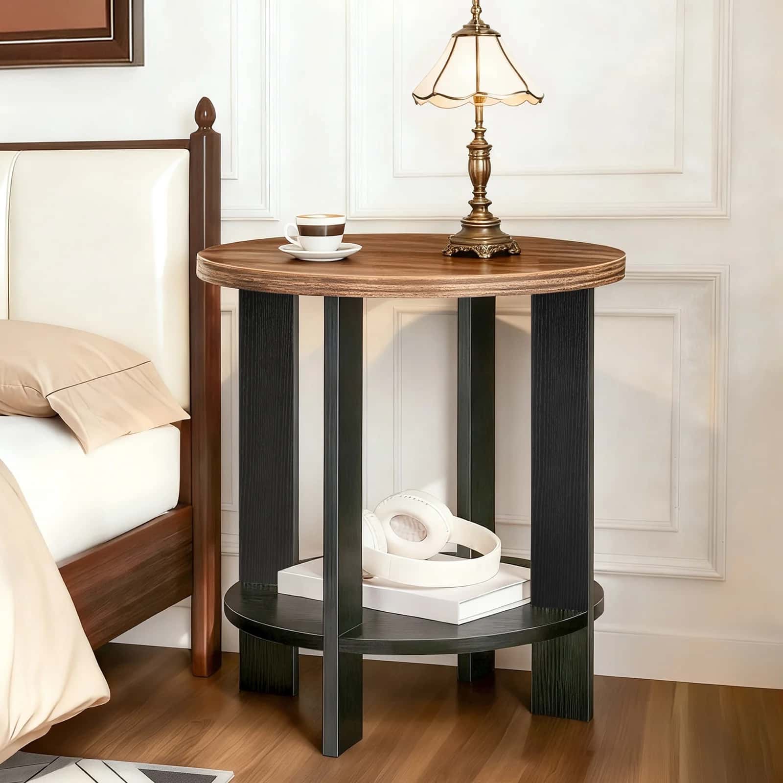 Round wooden side table with black legs next to a bed in a bedroom setting.